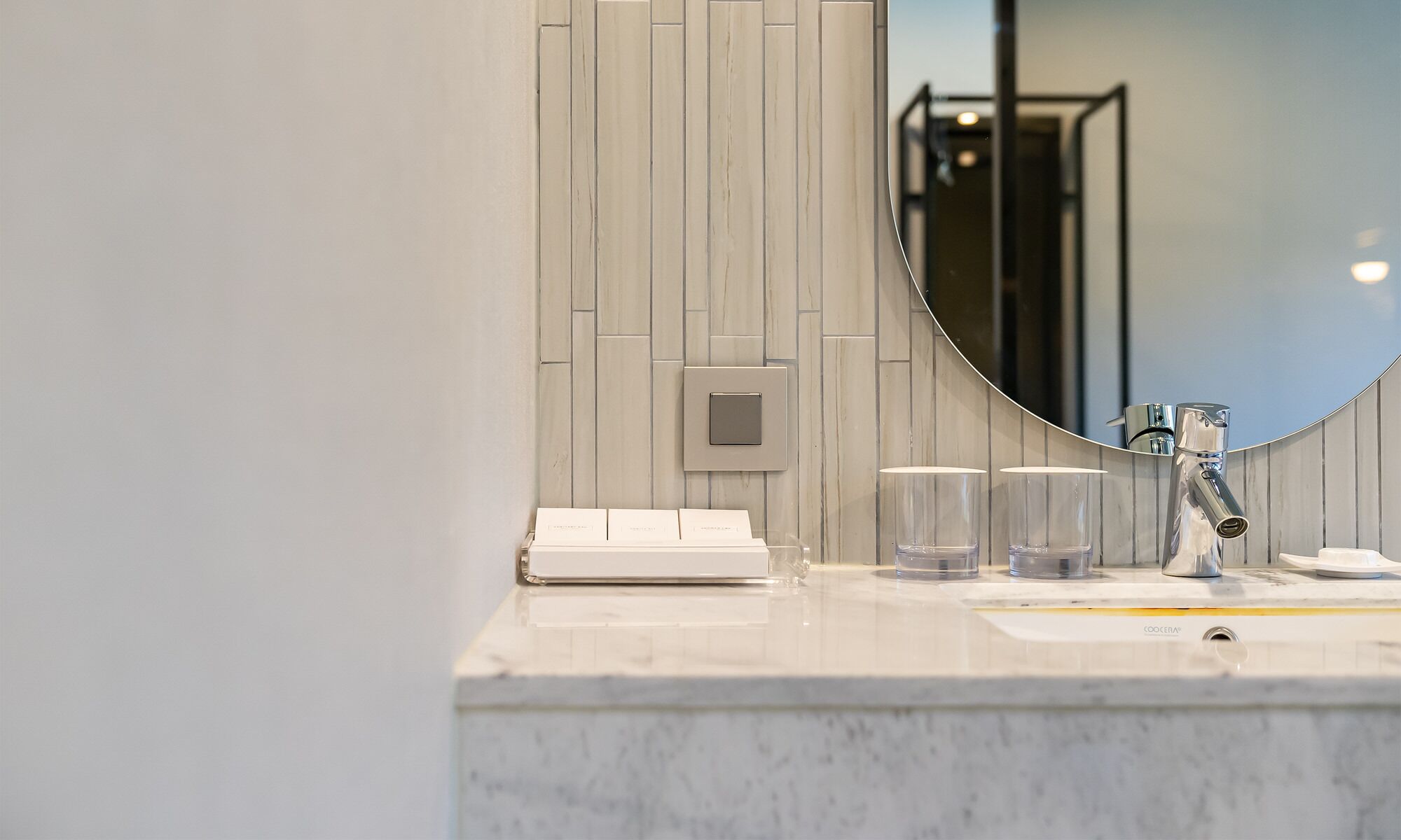A modern bathroom with a marble countertop, a round mirror, and a chrome faucet.
