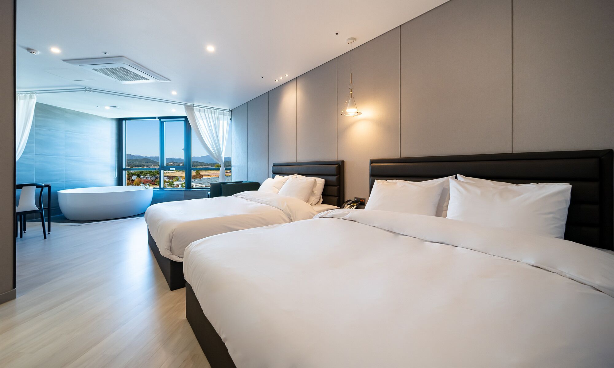 Una habitación de hotel moderna con dos camas grandes, un área de descanso con bañera y vistas al paisaje.