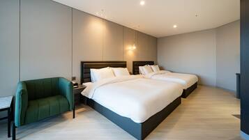 A modern hotel room with a large bed, a green armchair, and a desk with a chair.