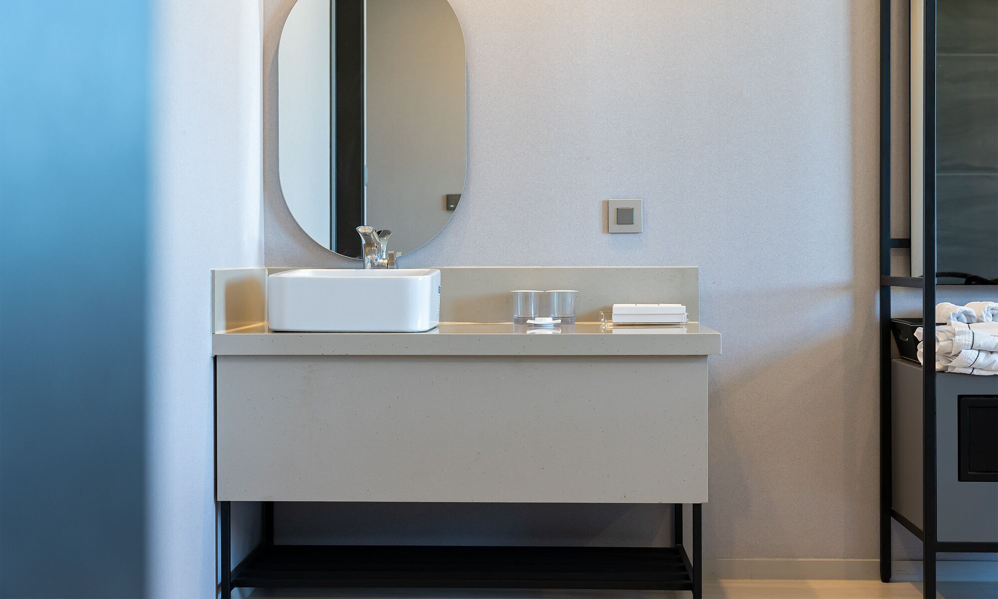A modern bathroom with a white sink, a round mirror, and a small shelf.