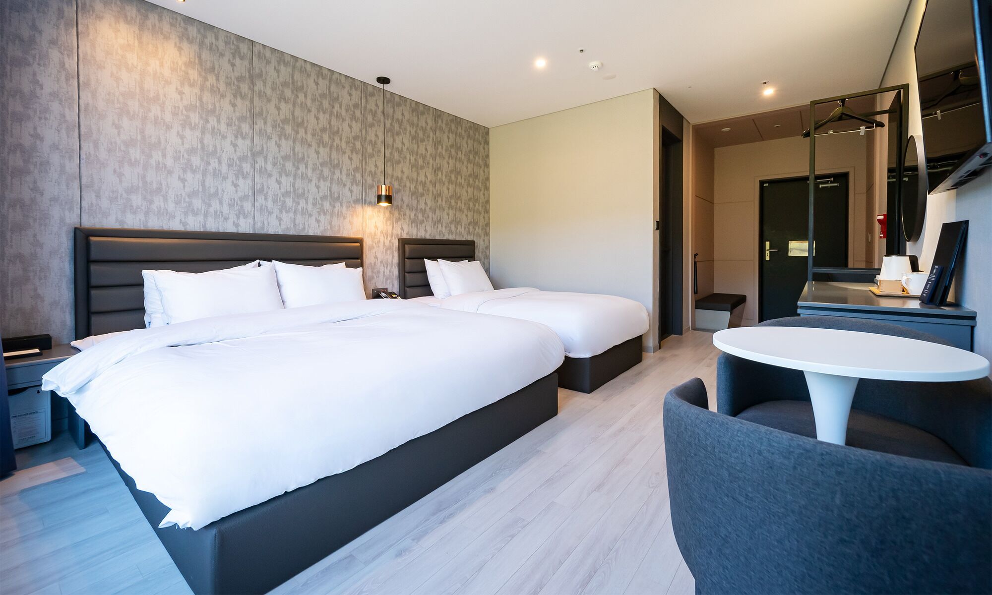 A modern hotel room with a large bed, bedside tables, a desk with a chair, and a small seating area.