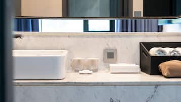 A modern bathroom with a large white sink, two glass tumblers, a towel rack, and a black storage box with towels.