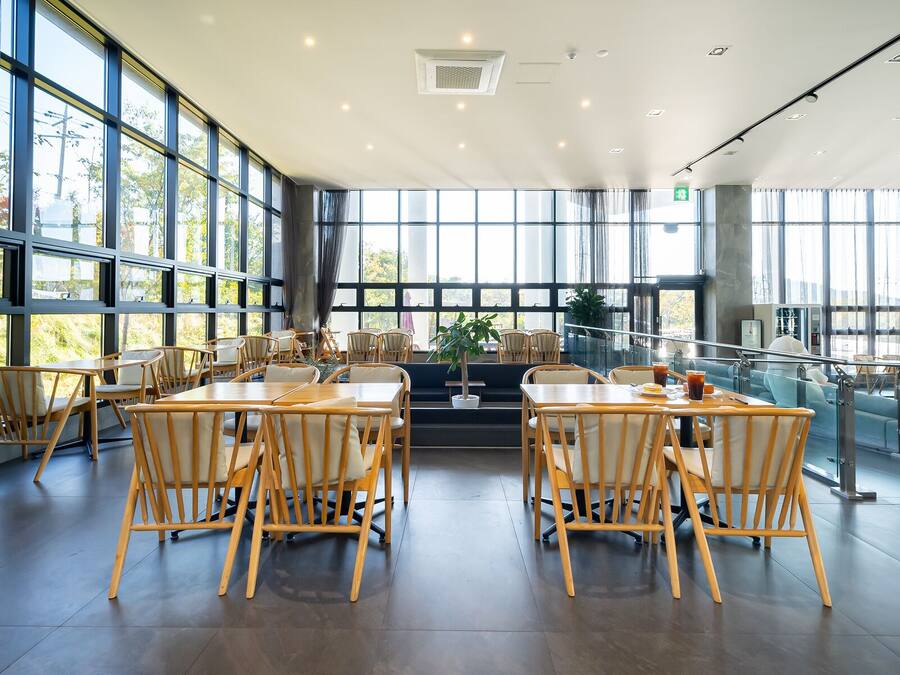 Un amplio espacio interior con ventanas grandes, mesas y sillas de madera, y una planta central.