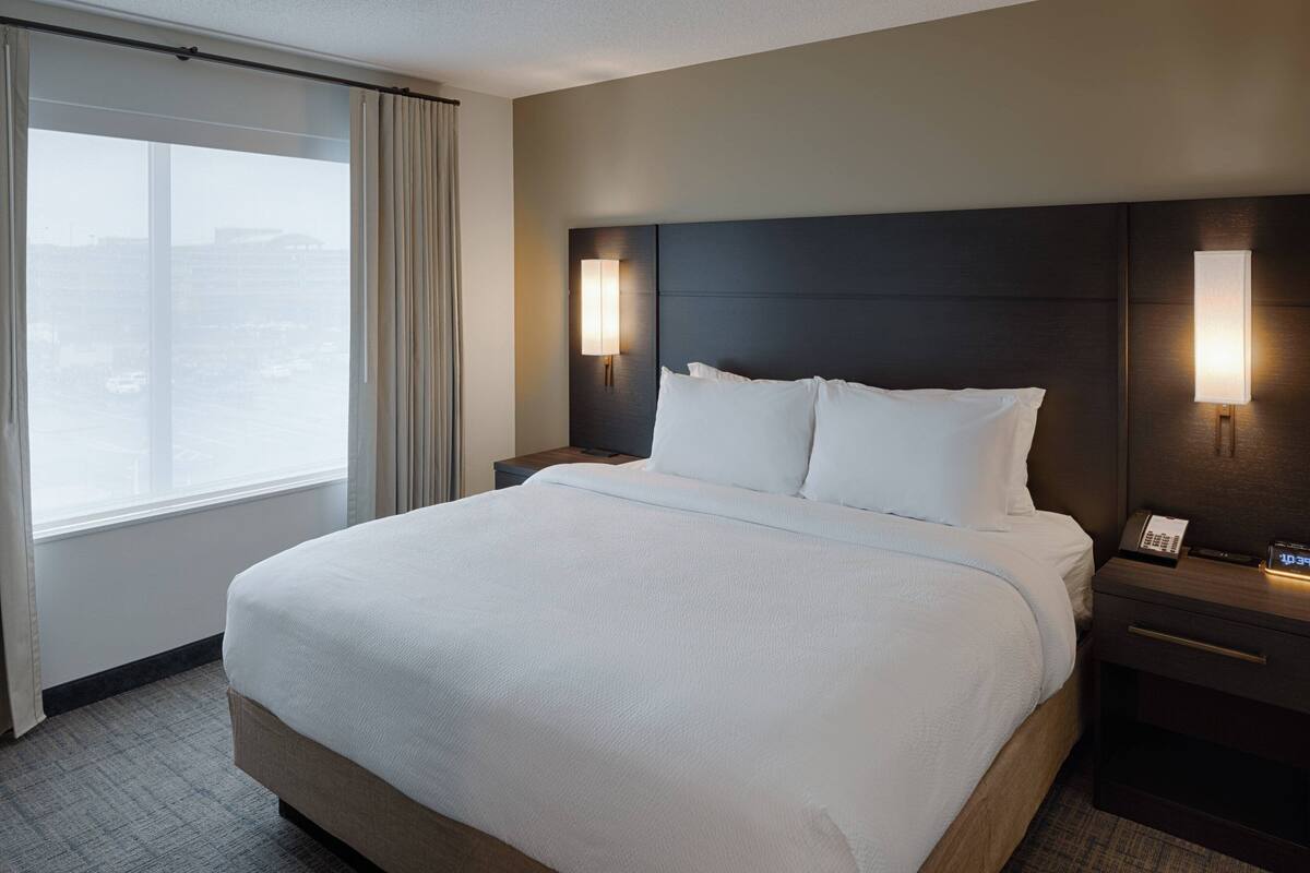 Habitación de hotel con una cama grande, dos mesitas de noche y un ventanal con cortinas.