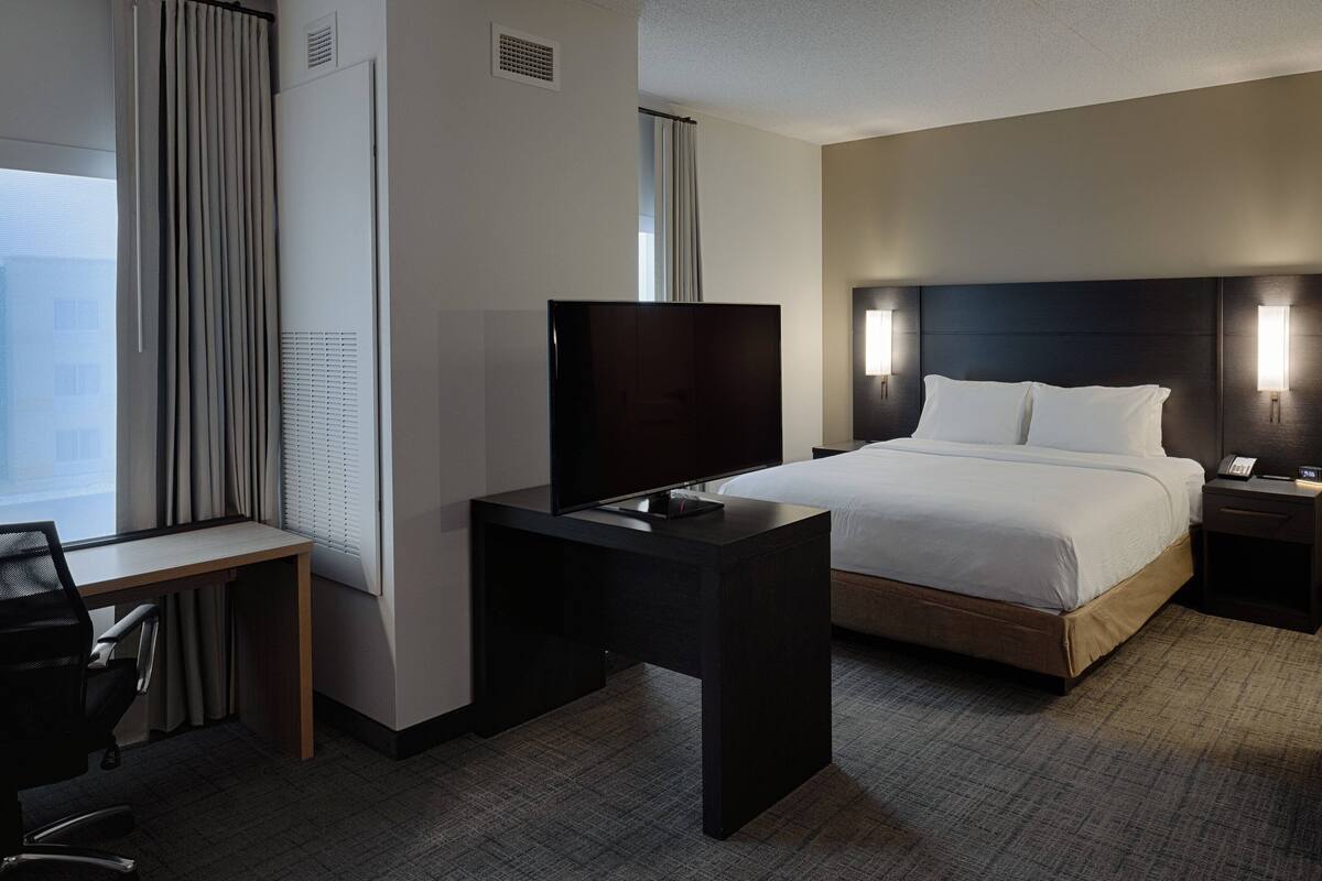 Habitación de hotel con una cama, un escritorio, un televisor y una ventana con cortinas.