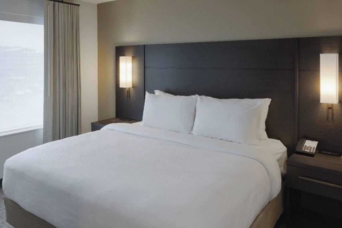 Una habitación de hotel con una cama grande, dos lámparas de noche, una mesita de noche con un teléfono y una ventana con cortinas.
