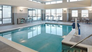 An indoor swimming pool with clear glass walls, a tiled floor, and a poolside area with chairs and a table. - Residence Inn by Marriott Columbus Airport (Columbus)