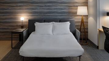 Habitació d'hotel moderna amb un llit, una tauleta de nit, una làmpada i un escriptori.