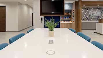 A modern conference room with a white table, blue chairs, a potted plant, a flat-screen TV, and a blue accent wall.
