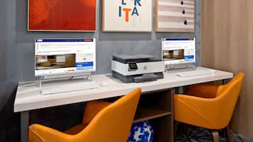 Un espace de travail équipé de deux ordinateurs de bureau, d’une imprimante et de deux chaises orange.