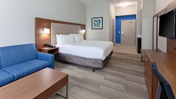Habitación de hotel con una cama, un sofá azul, una mesa de madera, un televisor y una puerta que da al baño.