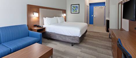 Habitación de hotel con una cama, un sofá azul, una mesa de madera, un televisor y una puerta que da al baño.