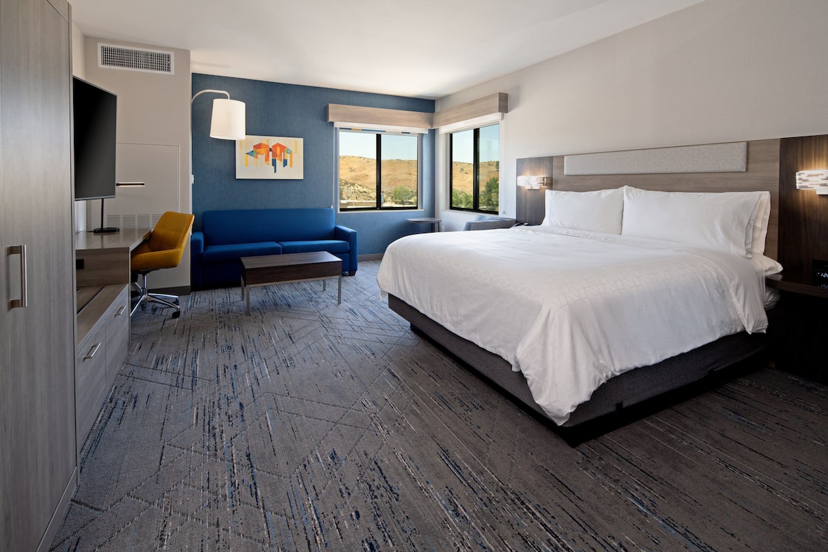 A modern hotel room with a large bed, a sofa, a TV, and a desk.