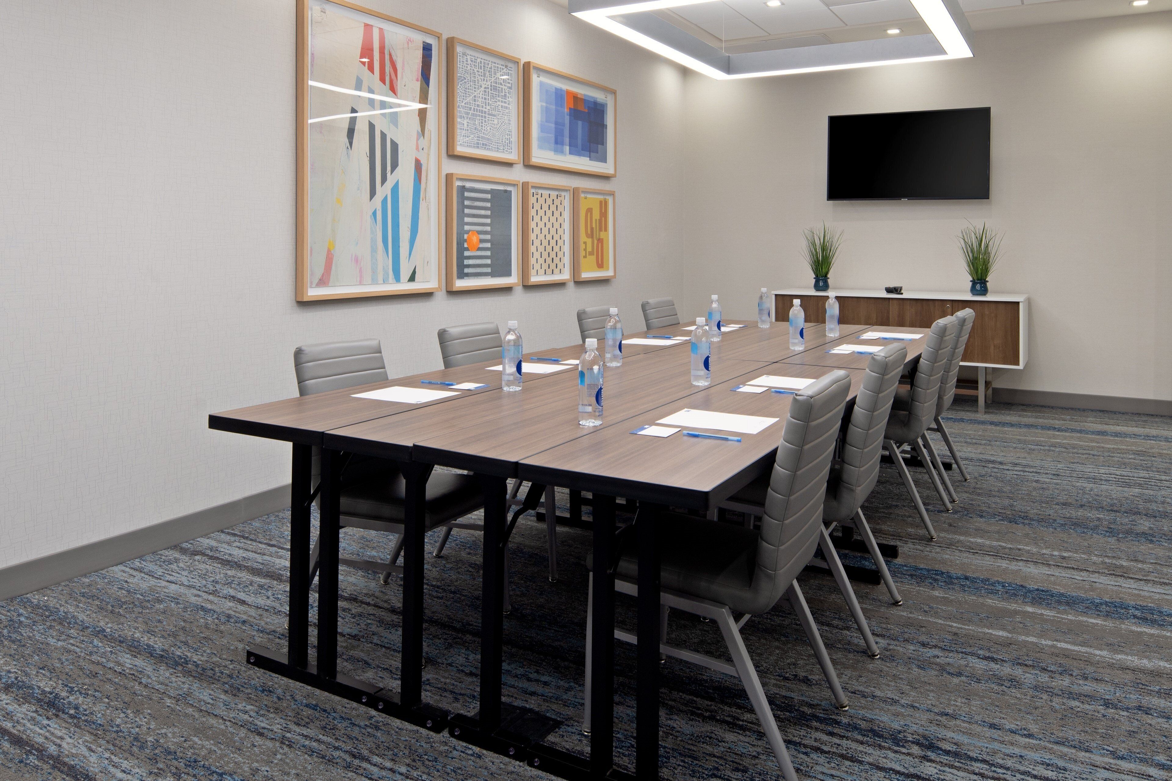 A conference room with a long table, chairs, water bottles, and a TV on the wall.