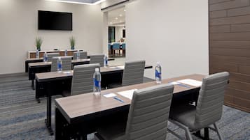 A conference room with multiple tables, chairs, and a flat-screen TV on the wall.