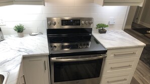 A kitchen with a stainless steel oven, white cabinets, and a marble countertop. - Stunning Niagara Warm,Cozy and Clean Suite Stay (2) (Welland)
