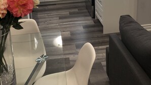 A modern kitchen with white cabinets, a stainless steel refrigerator, and a built-in oven. There is a dining area with a glass table and a vase of flowers. - Stunning Niagara Warm,Cozy and Clean Suite Stay (2) (Welland)