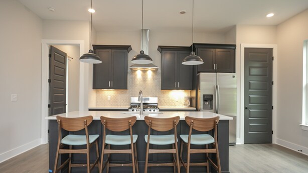 A modern kitchen with dark cabinets, a central island with bar stools, pendant lighting, and a stainless steel refrigerator.