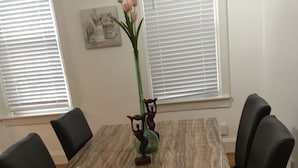 Een rechthoekige eettafel met een marmerlook blad, omringd door zes zwarte stoelen. Op de tafel staat een vaas met roze bloemen.