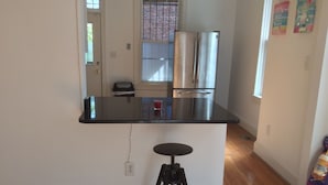 Een keuken met een zwart aanrecht, roestvrijstalen apparatuur, een zwarte stoel en een raam met jaloezieën.