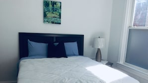 Een net opgemaakt bed met een witte deken, een donker hoofdbord en twee kussens.