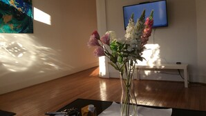 Een kamer met een houten vloer, een bloemenvaas, een schilderij aan de muur en een aan de muur bevestigde televisie.