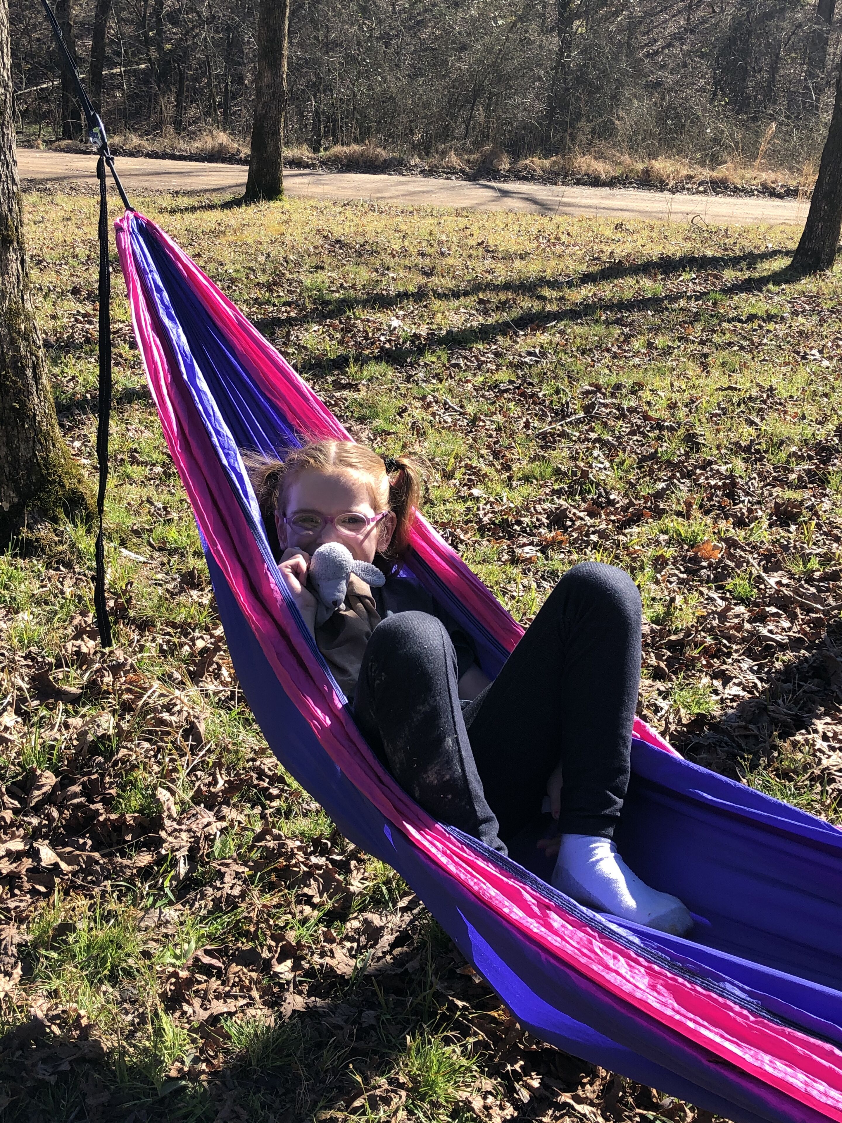 A hammock in a grassy area with trees in the background.