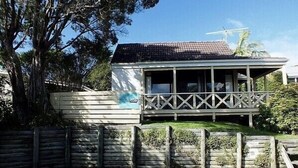 A two-story house with a balcony, a fenced yard, and a driveway. - Wharepekapeka - Russell Holiday Home (Russell)