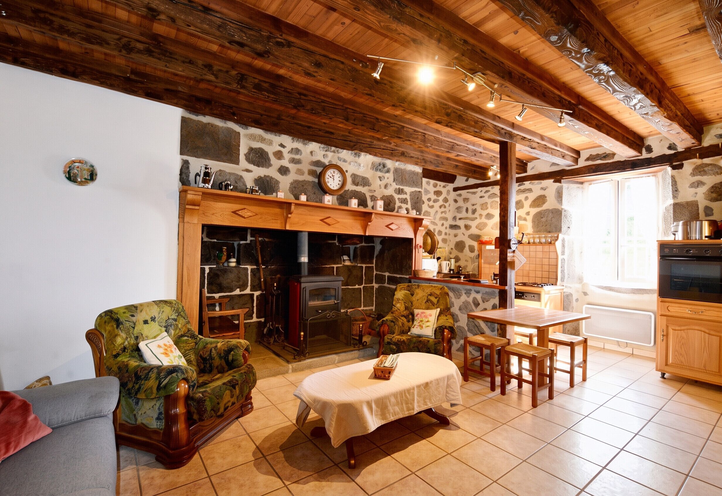 Ein gemütliches Wohnzimmer mit Kamin aus Stein, Holzmöbeln und einer Küchenzeile mit modernen Geräten.