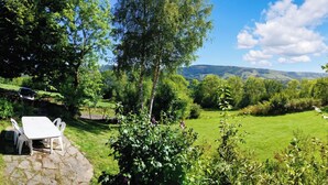 A garden with a stone table and chairs, surrounded by lush greenery and a view of distant hills.