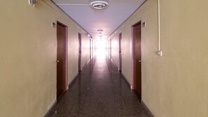 A long, narrow hallway with doors on both sides, a ceiling light, and a fluorescent light fixture.