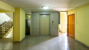 A hallway with a staircase on the left, an elevator in the center, and a wooden door on the right.
