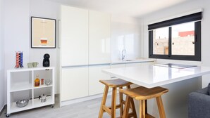 A modern kitchen with a white countertop, two wooden stools, a coffee machine, and a framed picture on the wall. - Cozy "Minimalist Apartment La Pecera" with Wi-Fi (Adeje)