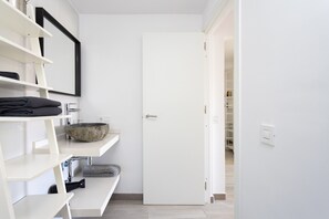 A modern bathroom with a white sink, a large mirror, and a door leading to a closet.