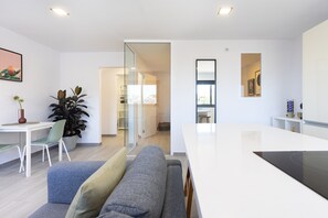 A modern living space with a sofa, a dining table, a kitchen area, and a glass partition.