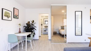 A modern room with a dining area, a large plant, a bed, and a bathroom visible through an open door. - Cozy "Minimalist Apartment La Pecera" with Wi-Fi (Adeje)