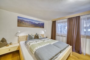 Une chambre à coucher avec un lit, une table de chevet, une lampe, une fenêtre avec des rideaux et un tableau au mur.