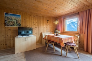 Un intérieur en bois avec une télévision, une table, des chaises, une fenêtre avec des rideaux et un tableau accroché au mur.