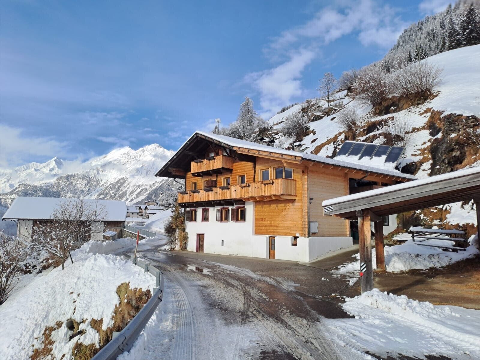 A wooden chalet with balconies, a snow-covered mountain backdrop, and a clear sky.