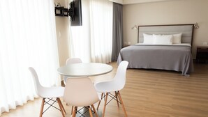 Camera d'albergo con un letto, un tavolo rotondo con sedie, una TV a parete e una finestra con tende.