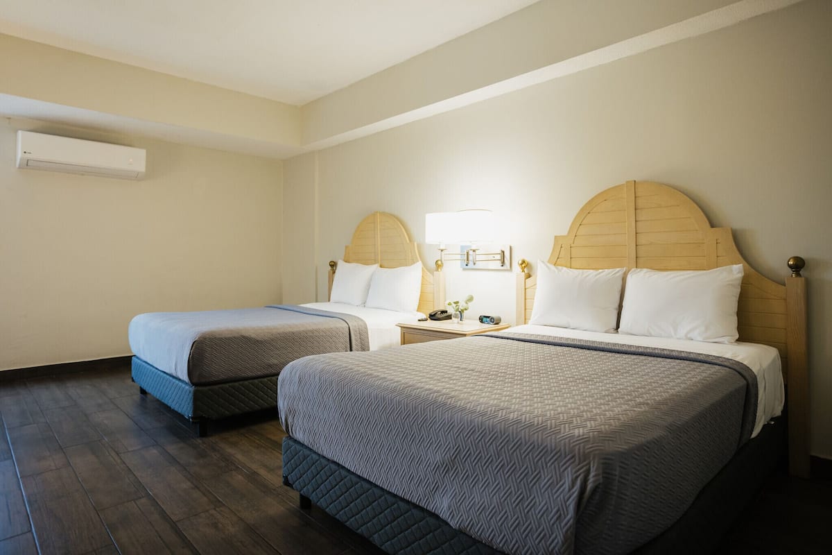 A hotel room with two beds, a nightstand, a lamp, and an air conditioning unit.