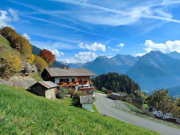 A mountain house with a road leading to it, surrounded by lush greenery and mountains.