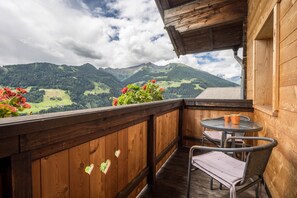 Un balcón de madera con mesa y sillas, con vistas a un paisaje montañoso.