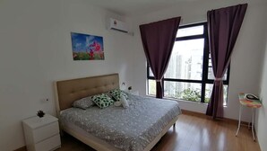 A bedroom with a bed, a nightstand, a small table, a window with curtains, and an air conditioner. - Forest City Staview Bay by Wastone (Gelang Patah)