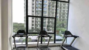 A gym with three treadmills aligned in a row, large windows with a view of high-rise buildings and greenery. - Forest City Staview Bay by Wastone (Gelang Patah)