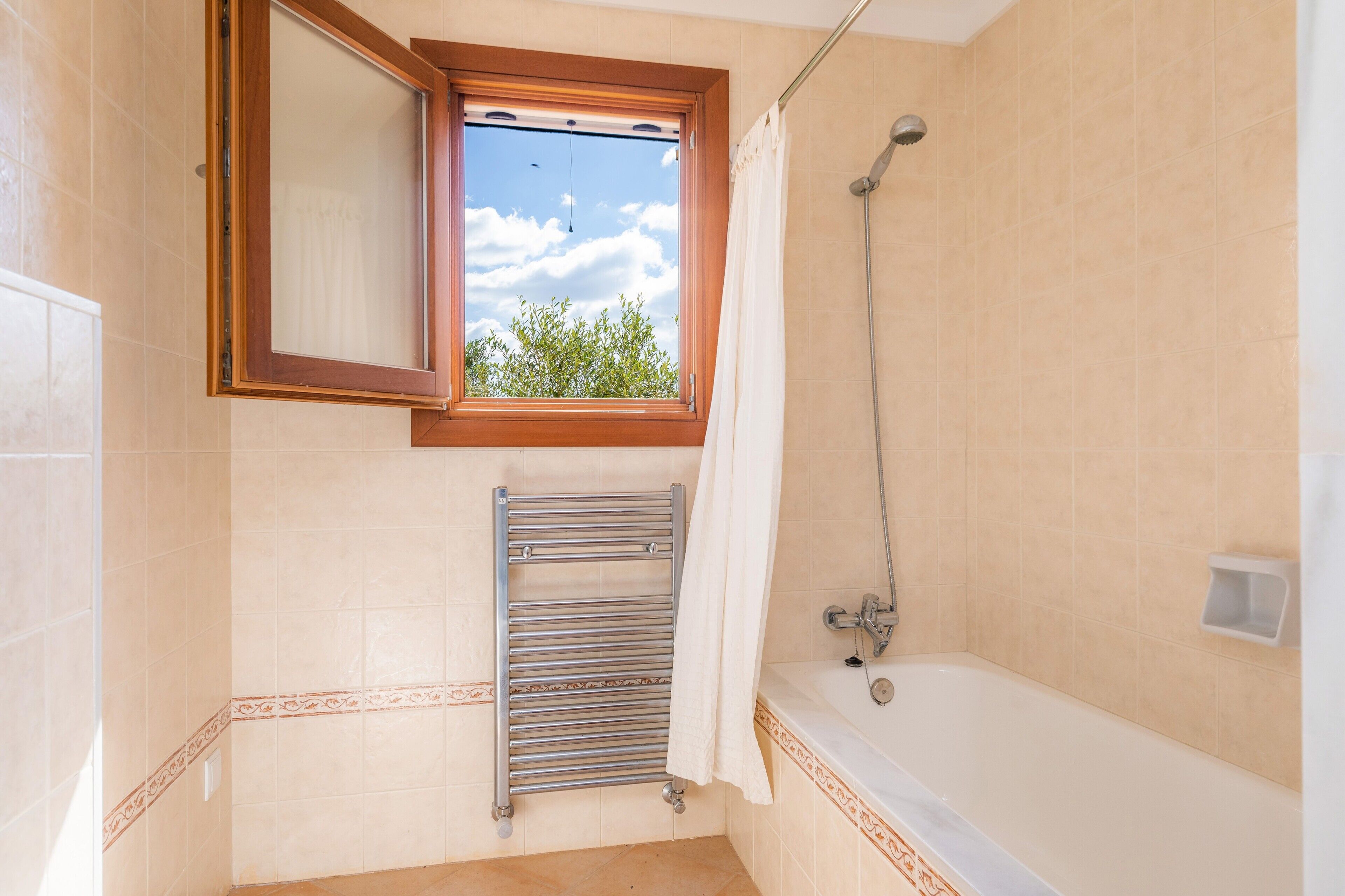 A bathroom with a bathtub, a shower, a window with a view of trees, and a towel rack.