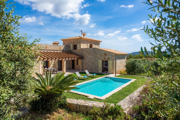 A stone villa with a swimming pool, outdoor seating, and a view of the surrounding landscape.