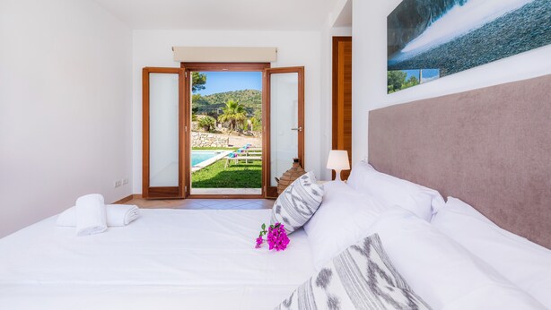 Une chambre avec un lit, une table de chevet, une lampe et une vue sur une piscine et un espace verdoyant.