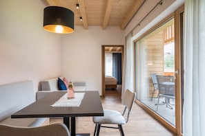 Un intérieur moderne comprenant une table à manger, des chaises, un canapé et une grande porte-fenêtre coulissante donnant sur un espace extérieur.
