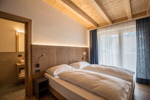 A bedroom with a wooden ceiling, a bed with white bedding, a bedside table, and a window with curtains.